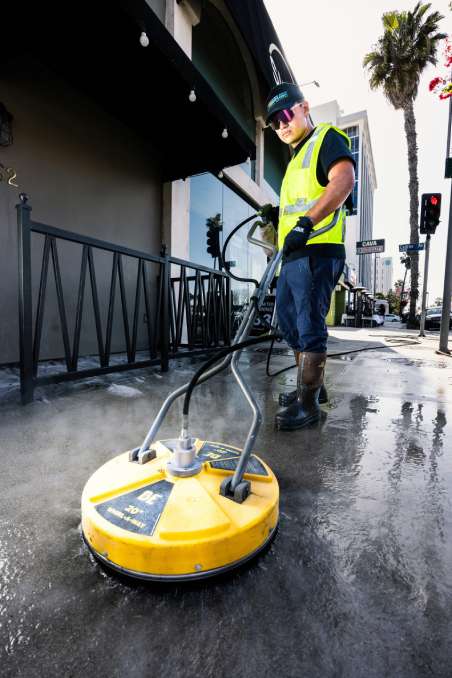 Worker power washing a sidewalk outdoors