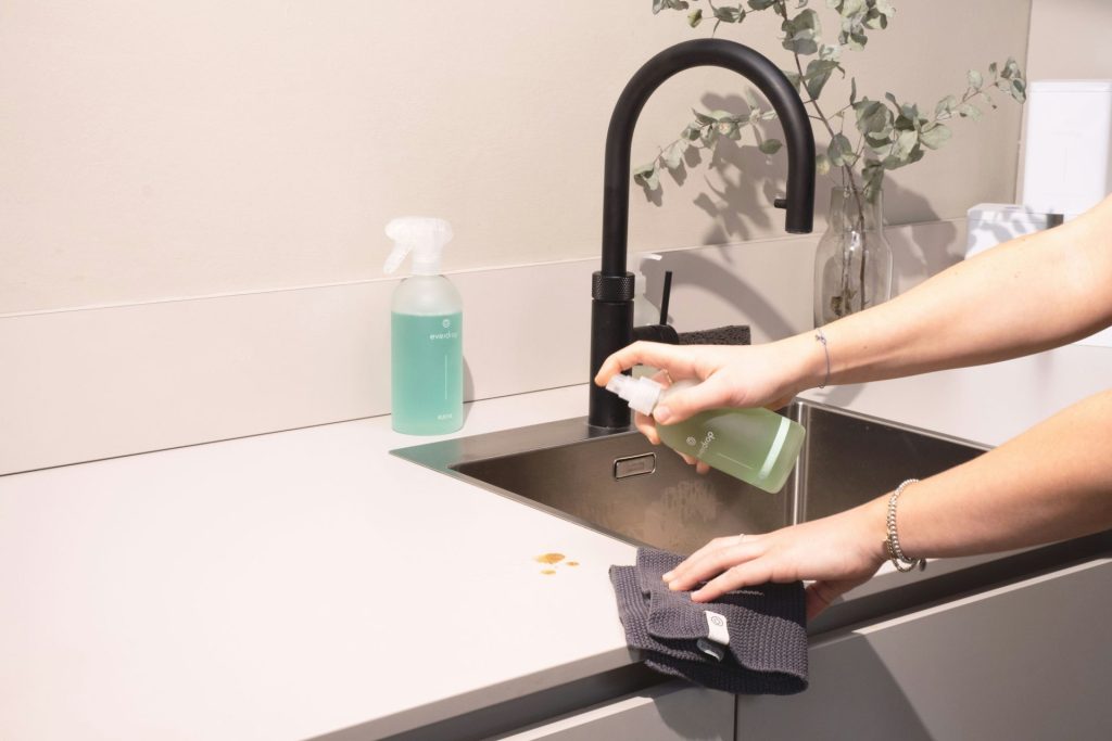 Cleaning a kitchen sink with green spray