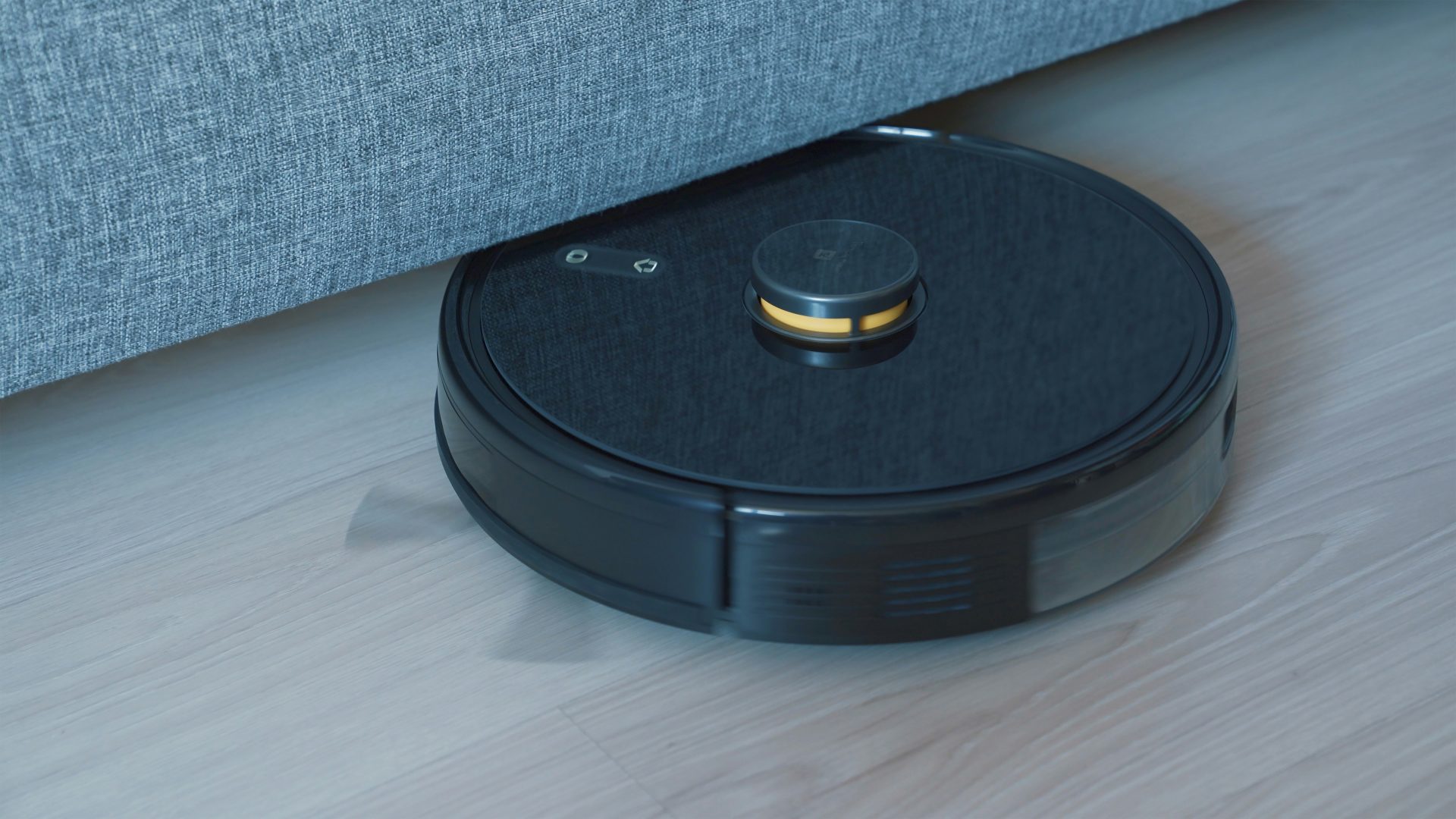 Black robot vacuum cleaning under a couch